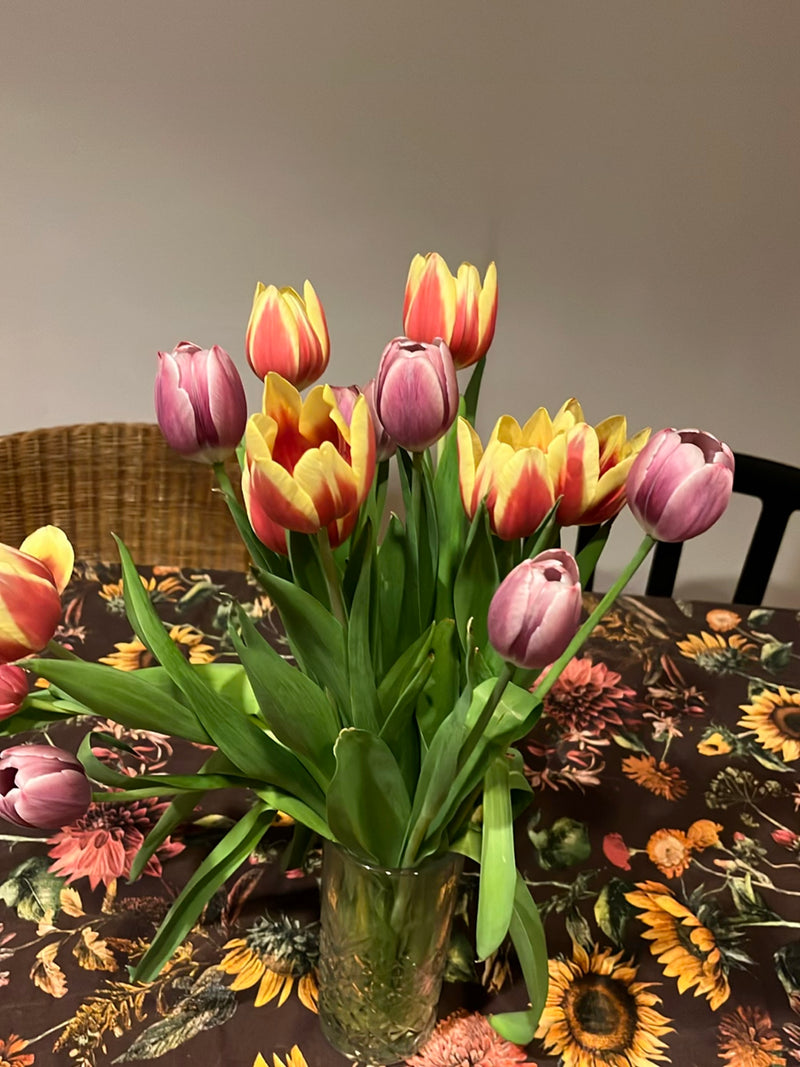 Un bouquet coloré de tulipes de jardin se trouve dans un vase en verre sur une table à motifs. Les fleurs affichent différentes couleurs comme le rouge, le j...