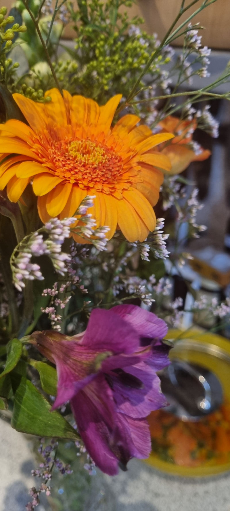 On peut voir une gerbera orange vif faisant partie d'un bouquet coloré. Les pétales caractéristiques et l'inflorescence en capitule sont bien visibles.