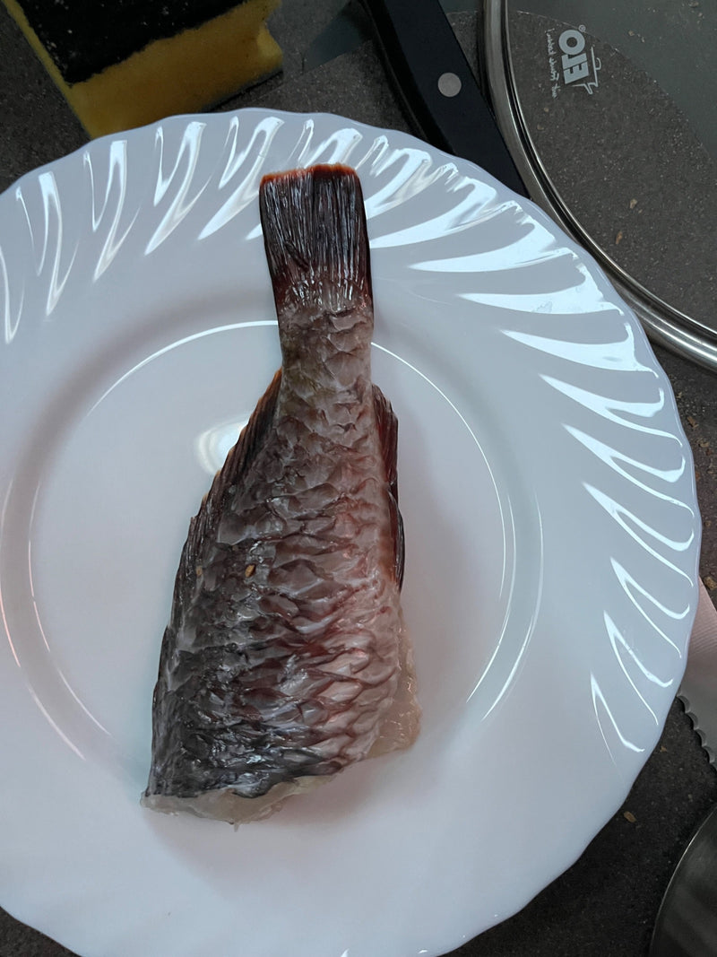 Un morceau de carpe avec des écailles distinctes et la nageoire caudale repose sur une assiette blanche.