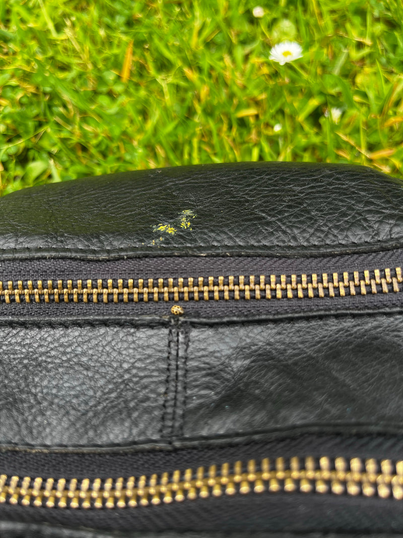 Une très petite cochenille à seize points se trouve sur un sac en cuir noir près de la fermeture éclair. Une prairie verte est visible floue en arrière-plan.